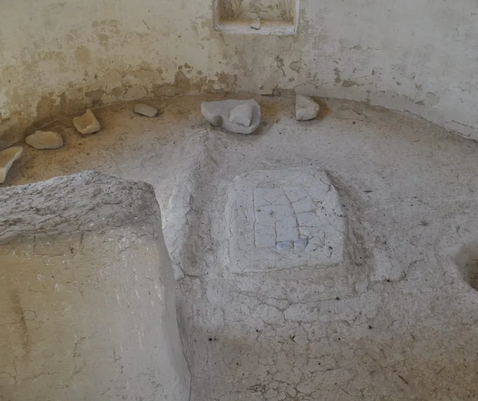 The inside of a round house — a curved plastered wall, a raised platform on the floor and small stones set around the base of the wall